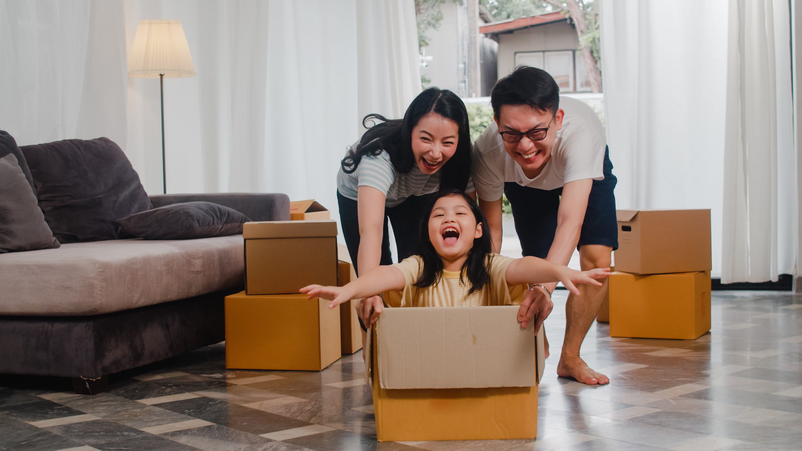 Asian Family pushing their daughter in moving box in new home
